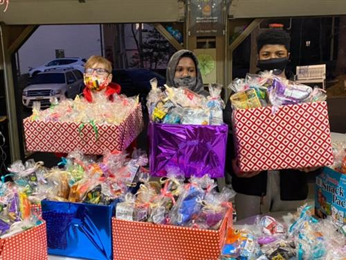 Three boys are holding wrapped boxes of snacks and cards for local workers and patients with COVID. 